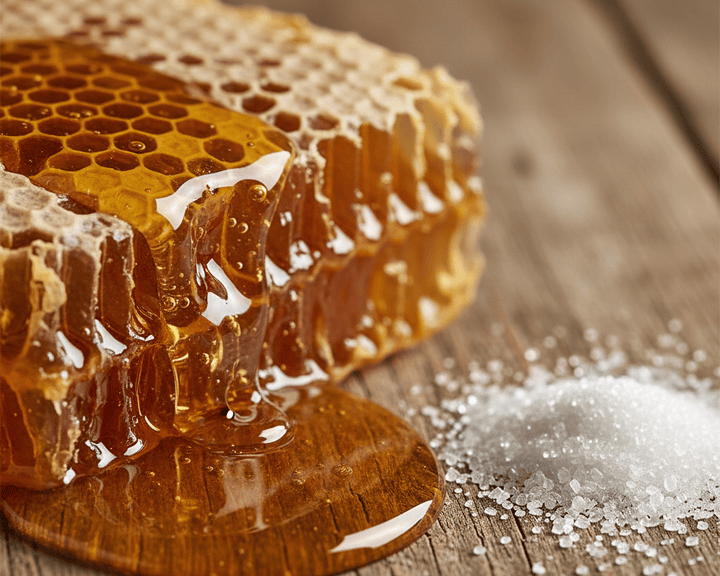 Raw honey dripping from comb next to white sugar